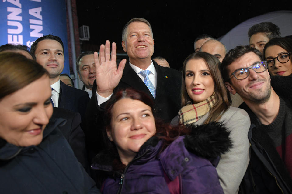 Romanian President Klaus Iohannis, centre, waves while posing with members of the media media after exit polls were published, in Bucharest, Romania, Sunday, Nov. 24, 2019. An exit poll by the IRES independent think tank has predicted Iohannis getting 66.5 % of the votes, with 33.5% for Social Democratic Party leader Viorica Dancila, a former prime minister. (AP Photo/Andreea Alexandru)