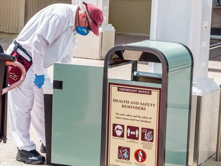 Janitor emptying a mint green trash can with a health and safety sign.