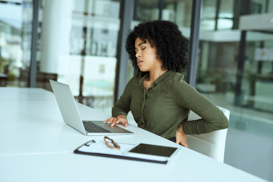 Shot of a young businesswoman experiencing back pain while using a laptop at her desk in a modern office