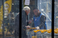 Raffat Altekrete, right, talks to an elderly man when battling the coronavirus one shopping cart at a time using a disinfecting spray outside a supermarket in Ter Apel, north-eastern Netherlands, Tuesday, March 31, 2020. The Iraqi migrant, armed with latex gloves, a cleaning rag and a spray bottle of disinfectant is also aiming to express his gratitude and win hearts in a small Dutch community that hosts the Netherlands' biggest asylum seeker center. (AP Photo/Peter Dejong)