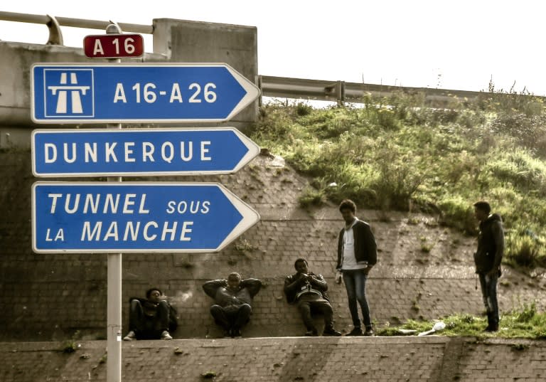 Migrants sit watching lorries driving towards the Calais port where ferries sail to Britain