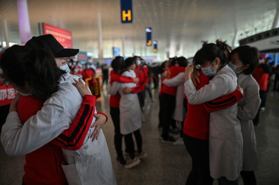 Medical staff from Jilin Province (in red) hug nurses from Wuhan after working together during the COVID-19 coronavirus outbreak during a ceremony before leaving as Tianhe Airport is reopened in Wuhan in China's central Hubei province on April 8, 2020. - Thousands of Chinese travellers rushed to leave COVID-19 coronavirus-ravaged Wuhan on April 8 as authorities lifted a more than two-month prohibition on outbound travel from the city where the global pandemic first emerged. (Photo by Hector RETAMAL / AFP) (Photo by HECTOR RETAMAL/AFP via Getty Images)