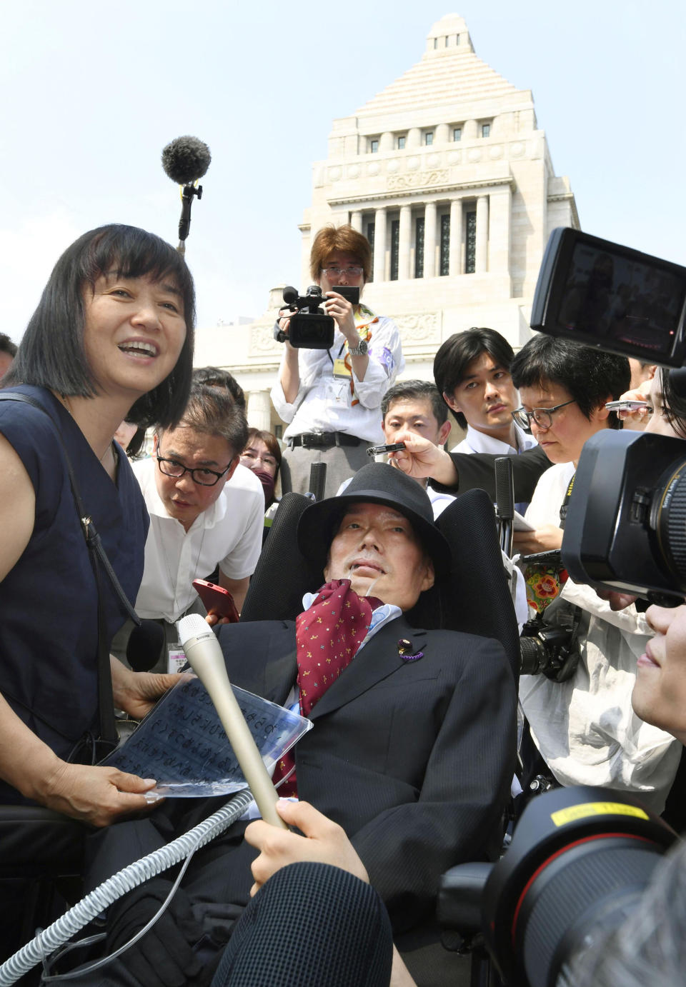 Newly-elected lawmaker Yasuhiko Funago in a wheelchair is surrounded by journalists as he arrives at the parliament's building, background, to attend an extraordinary session of the upper house in Tokyo Thursday, Aug. 1, 2019. Japan’s parliament convened after elections and a minor renovation at the upper house. Funago, who has Amyotrophic Lateral Sclerosis, a progressive neurological disease known as ALS, won the July 21 elections, representing an opposition group. (Daisuke Suzuki/Kyodo News via AP)