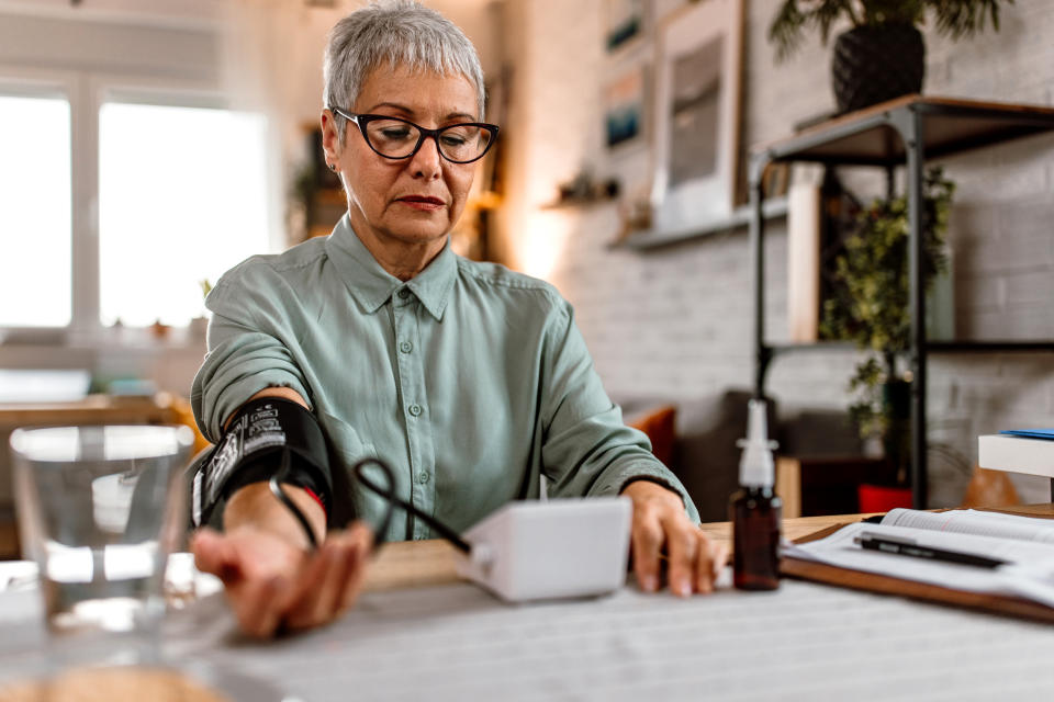 A senior woman sits at the table and measures blood pressure at her home.