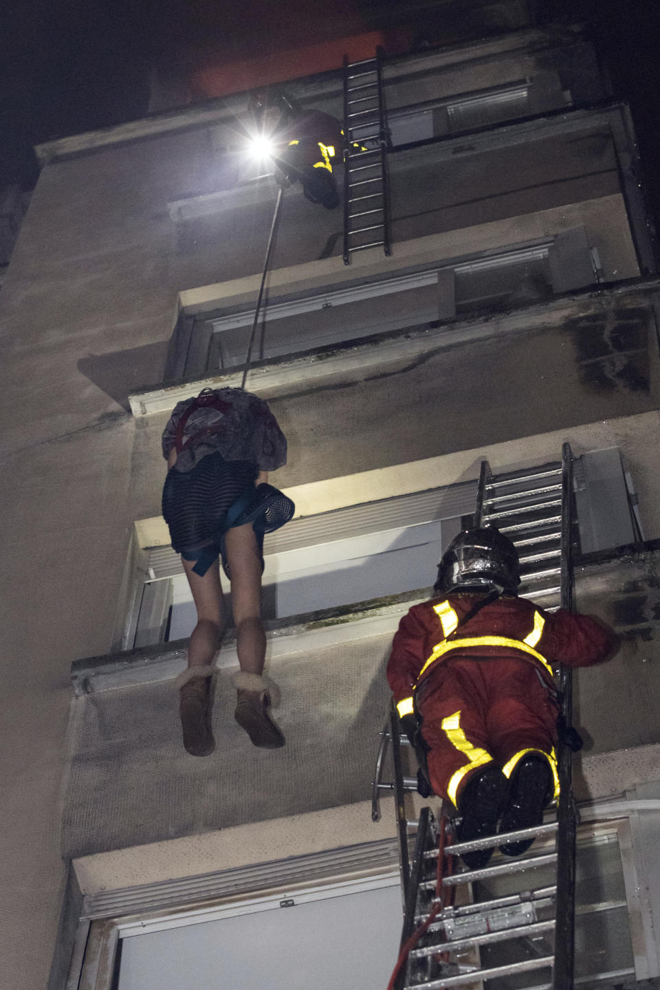 In this image provided on Tuesday, Feb. 5, 2019 by the Brigade de Sapeurs-Pompiers de Paris (Paris Fire Brigade) firefighters use a rope to evacuate a resident after a fire engulfed an apartment building , in Paris, France. A fire in a Paris apartment building early Tuesday that authorities suspect was an arson attack killed seven people and sent residents fleeing to the roof or climbing out their windows to escape. (Benoit Moser/BSPP via AP)
