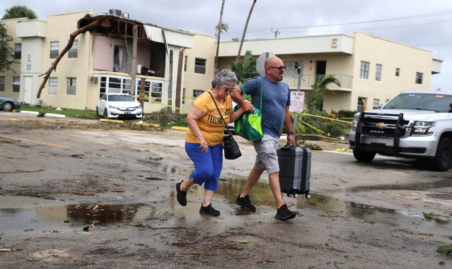 Kings Point resident Maria Esturilho is escorted by her son Tony Esturilho as they leave behind the damage from an overnight tornado spawned from Hurricane Ian in Delray Beach, Fla., on Wednesday, Sept. 28, 2022. (Carline Jean/South Florida Sun-Sentinel via AP)
