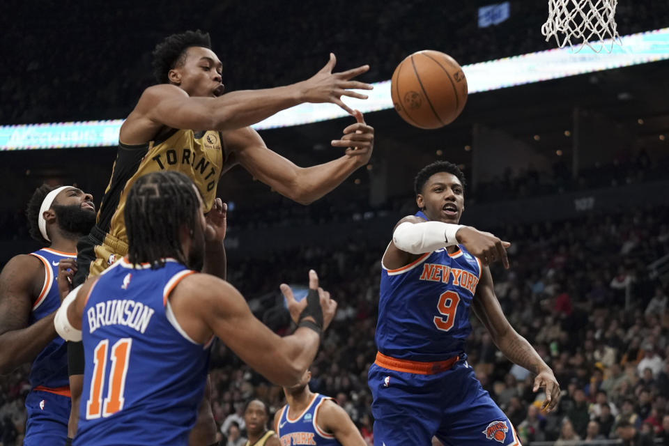 Toronto Raptors forward Scottie Barnes (4) jumps to shoot while guarded by New York Knicks guard RJ Barrett (9), right, and guard Jalen Brunson (11) during first-half NBA basketball game action in Toronto, Friday, Dec. 1, 2023. (Arlyn McAdorey/The Canadian Press via AP)