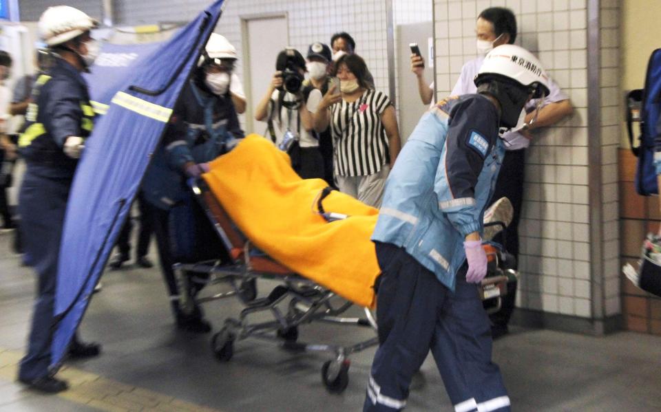 Rescuers carry an injured passenger on stretcher at Soshigaya Okura Station after stabbing on a commuter train, in Tokyo Friday night, Aug. 6, 2021 - AP