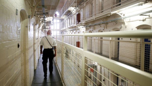 A prison officer, facing away from the camera, walks down a gantry on a prison wing