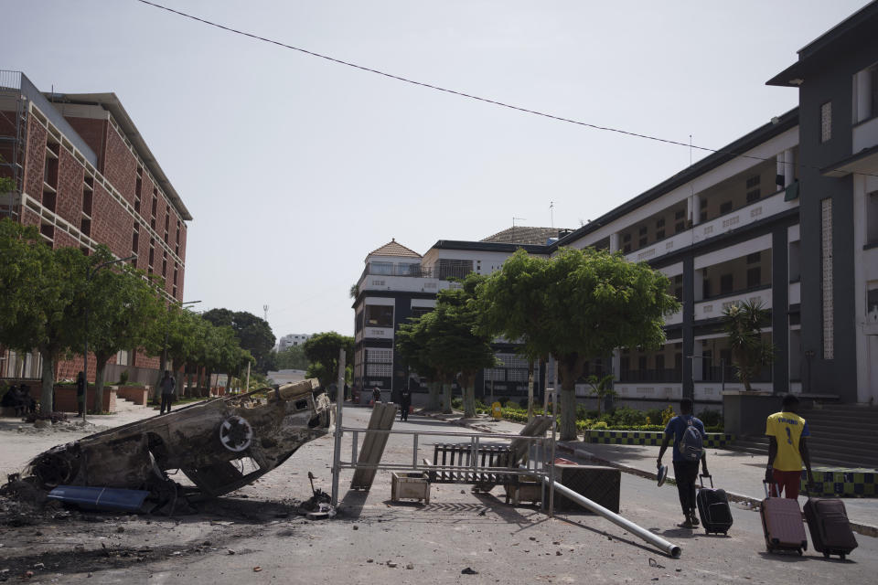 Carrying their belongings students walk past a burned car as they leave the campus of the Cheikh Anta Diop University after authorities ordered the institution to be closed until further notice in Dakar, Senegal, Friday, June 2, 2023. Clashes between police and supporters of Senegalese opposition leader Ousmane Sonko left nine people dead, the government said Friday, with authorities issuing a blanket ban on the use of several social media platforms in the aftermath of the violence. (AP Photo/Leo Correa)