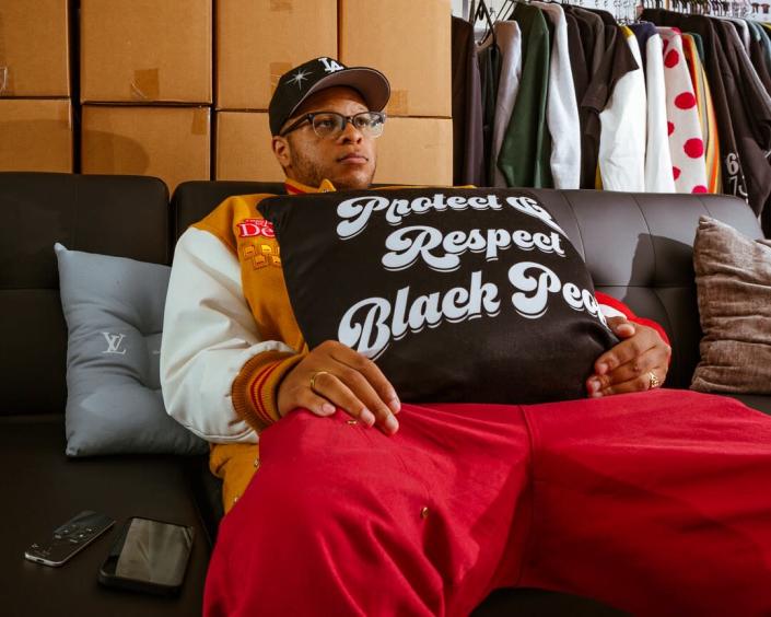 A person leans back on a couch, holding a pillow that says &quot;Protect and respect Black people.&quot;