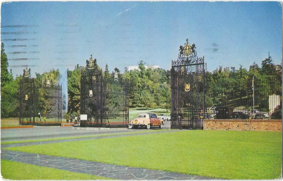 A car enters the gates of a cemetery with a wide green lawn.