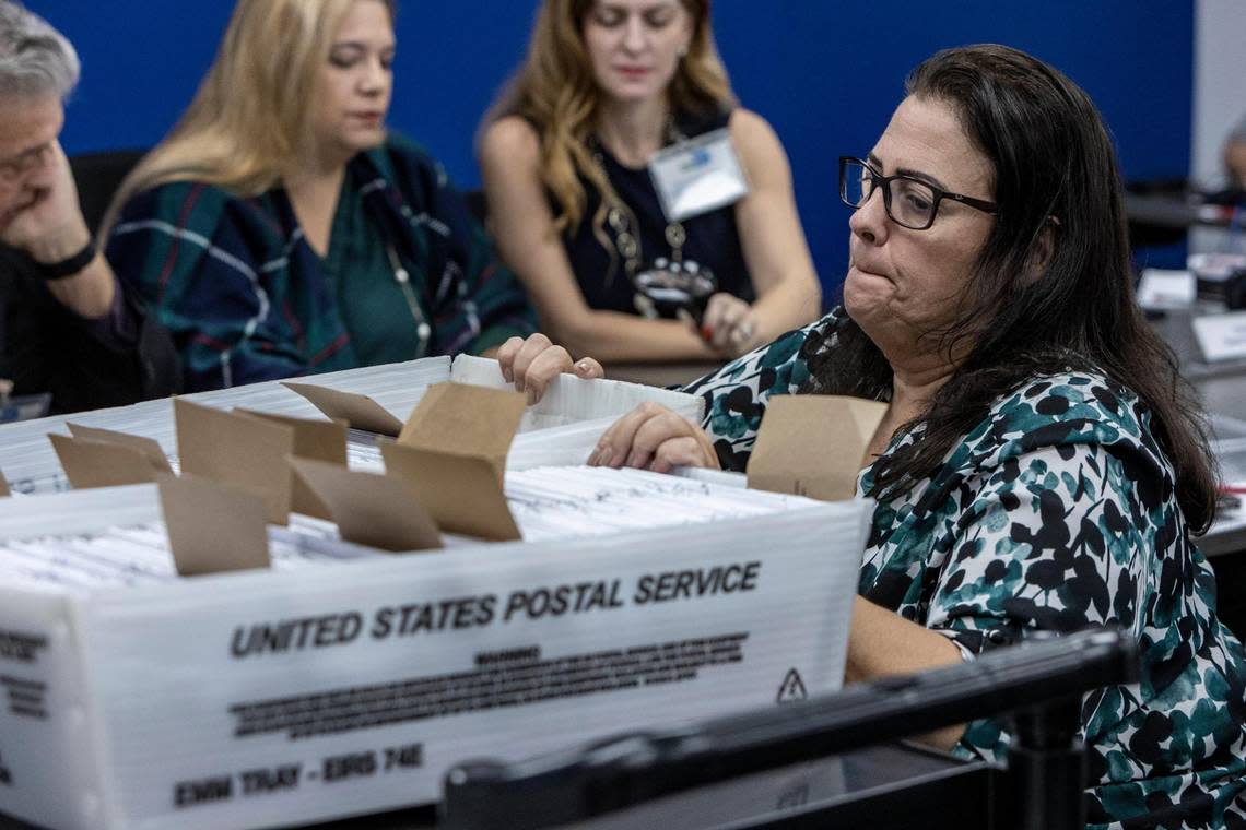 A worker for the Miami-Dade County Elections Department accommodates baskets of vote-by-mail ballots that need to be checked by the Canvassing Board as Judge Luis Perez Medina, left, Judge Victoria Ferrer and Miami-Dade County Supervisor of Elections Christina White examine signatures in Doral on Oct. 20, 2022.