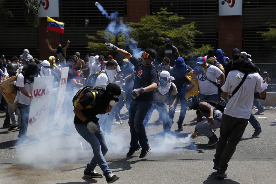 Anti-government protesters throw teargas canisters back at the police in Caracas