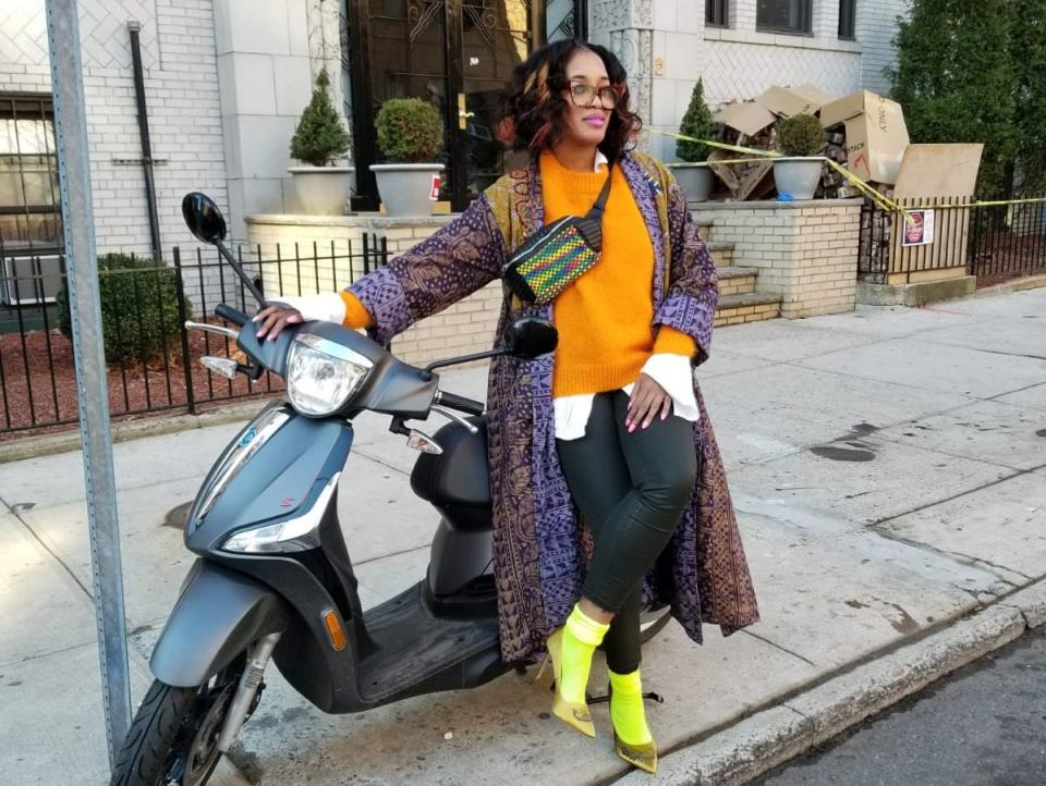 Sandra wearing a cross body fanny pack while posing in front of moped