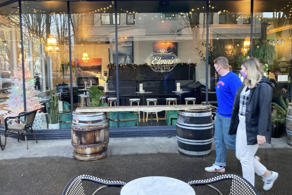 A couple walks past a wine bar in McMinnville, Ore., on Thursday, Dec. 9, 2021. Like many other towns in the U.S., McMinnville was hit by the opioid epidemic, leaving overdoses, addiction, homelessness and wrecked families in its wake. States, counties and cities are on the precipice of receiving billions of dollars in the second-biggest legal settlement in U.S. history. (AP Photo/Andrew Selsky)