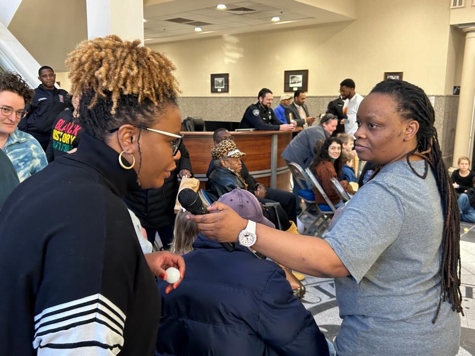 Nadia Beard holds the microphone up to Angela Harvey and asks her to read the word labeled on her ping pong ball as part of Beard's exercise involving the audience at City Hall's third Black History Month event on Friday Feb. 17.