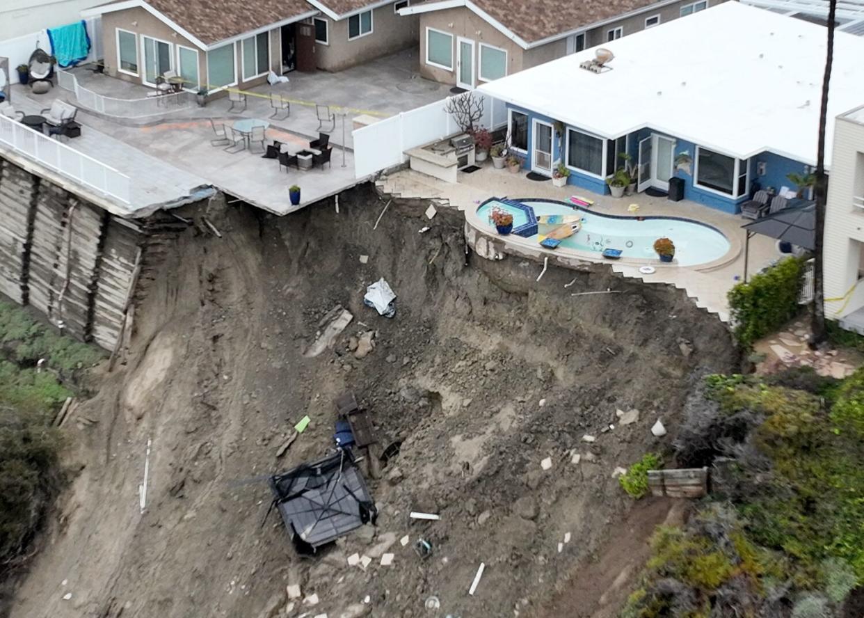 An aerial view of four cliff-side, ocean-view apartment buildings with one standing dangerously over a washed-0ut hill.