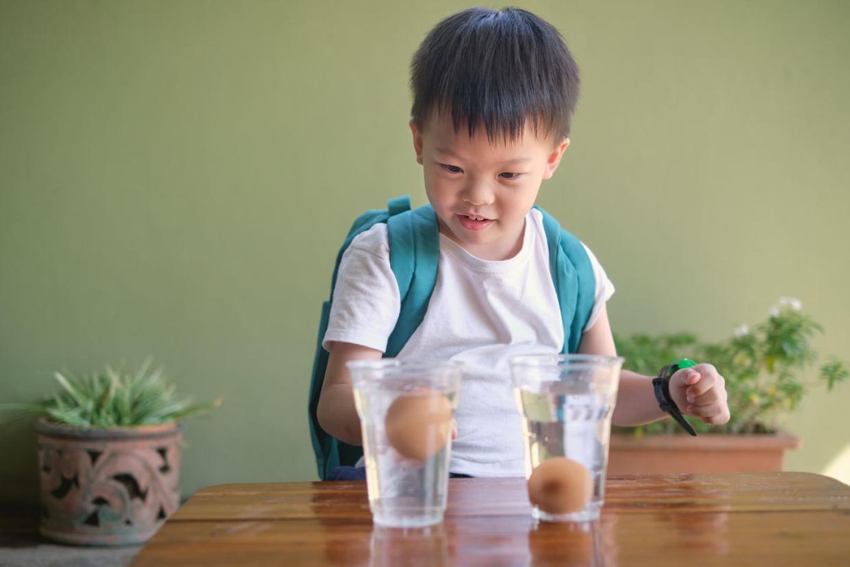 happy asian school kid studying science, doing fun and easy floating egg science experiment to learn about the density of salt water effect to floating and sinking of the eggs