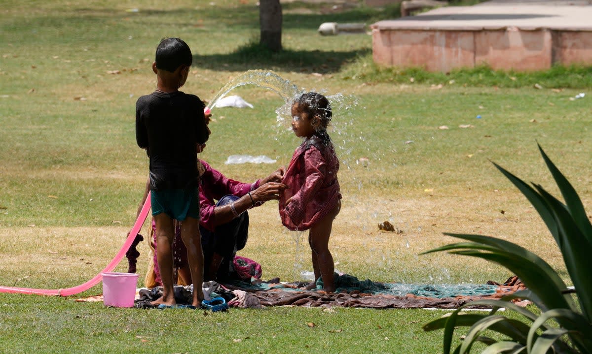 A family cools themself in a park using an irrigation water pipe as northern Indian continues to reel under intense heat wave in Lucknow, Uttar Pradesh on Wednesday, April 19, 2023 (AP)