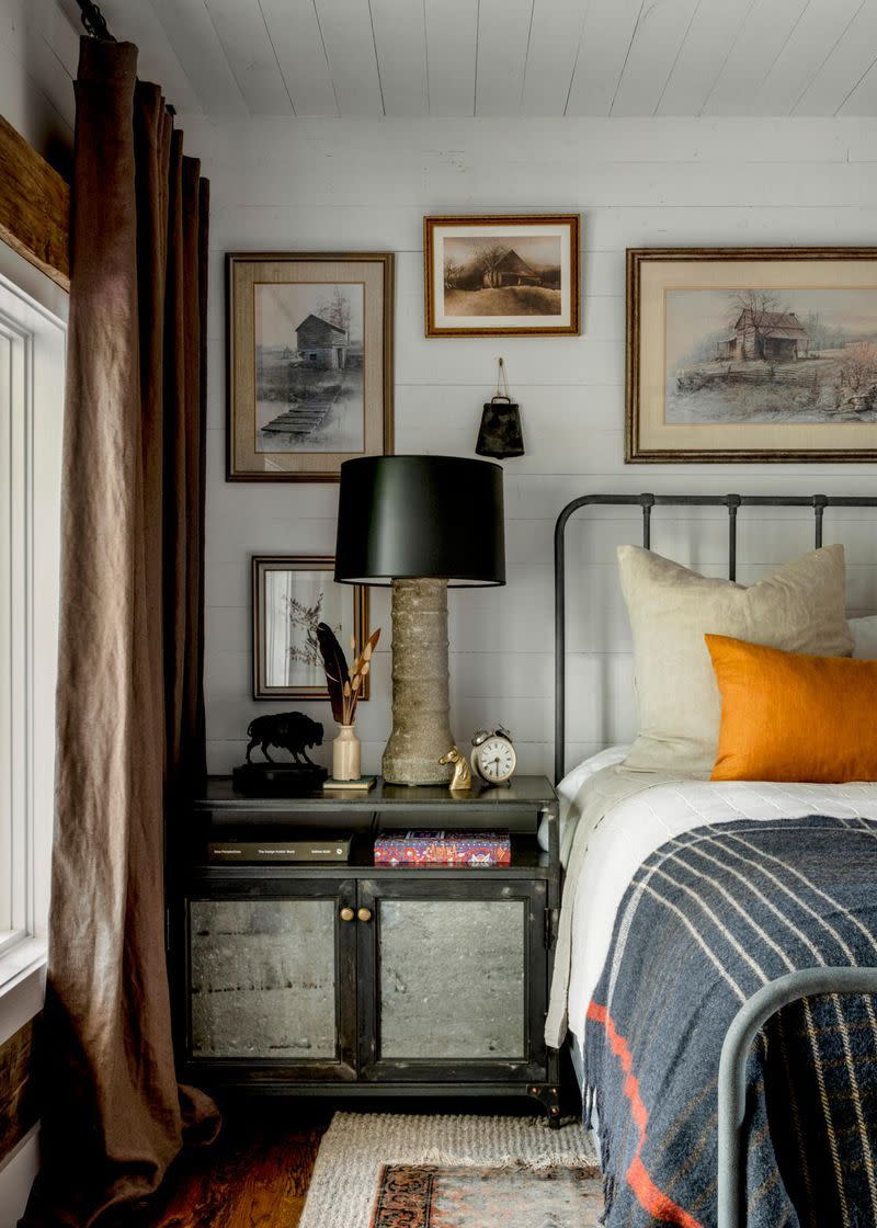 a cowbell found on the property and a collection of prints and paintings of old barns and houses adorn the wall in one of the cabin bedrooms and the walls semi transparent white stain shows off a bit of the wood grain of the tongue and groove pine