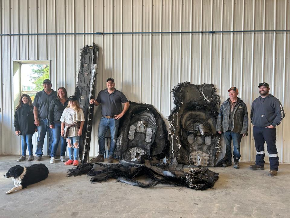 Barry Sawchuk, second from right, stands with space debris that landed on his farm and other farms in the area.