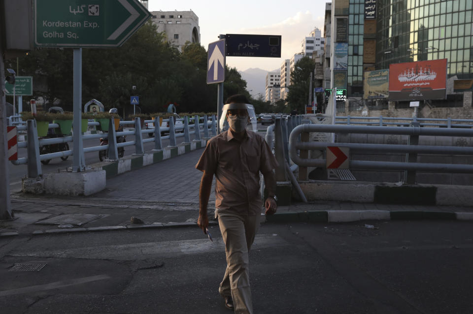 A man wearing protective face mask and shield to help prevent the spread of the coronavirus crosses a street in central Tehran, Iran, Sunday, Aug. 8, 2021. Iranians are suffering through yet another surge in the coronavirus pandemic — their country's worst yet — and anger is growing at images of vaccinated Westerners without face masks on the internet or on TV while they remain unable to get the shots. (AP Photo/Vahid Salemi)