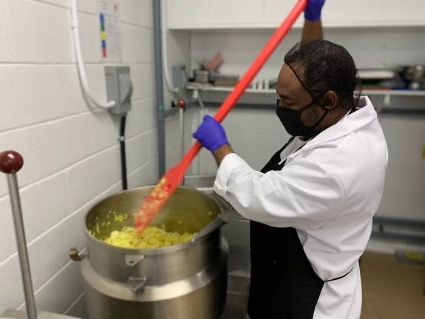 Karl Thomas, the operations manager at Shivani's Kitchen, stirs a large pot of onions as the kitchen produces a vegan sauce.  