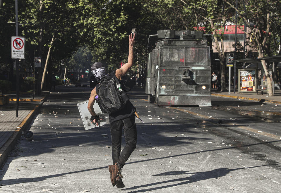 An anti-government protester throws a rock at a police water cannon during a protest in Santiago, Chile, Wednesday, Nov. 6, 2019. Chile's president Sebastian Pinera announced he is sending a bill to Congress that would raise the minimum salary, one of a series of measures to try to contain nearly three weeks of anti-government protests. (AP Photo/Esteban Felix)