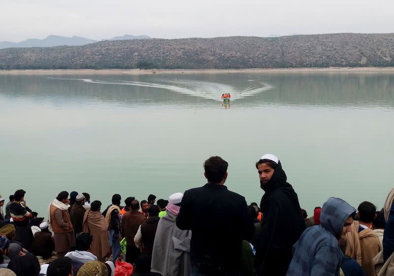 People gather as rescue workers search for the victims, after a boat carrying religious school students capsized in Tanda lake in Kohat