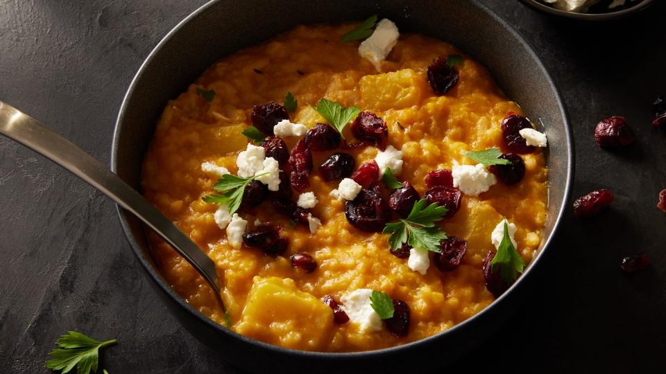 baked pumpkin risotto in a black bowl topped with cheese and dried cranberries