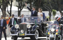 Flanked by first lady Michelle Bolsonaro, Brazil's President Jair Bolsonaro waves as he rides in an open car after his swearing-in ceremony, in Brasilia, Brazil, Tuesday, Jan. 1, 2019. (AP Photo/Andre Penner)