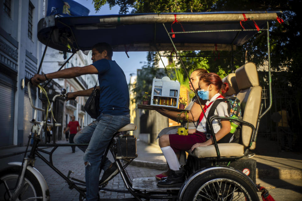 Una niña viaja a la escuela acompañada de su madre cargando su trabajo escolar en un bicitaxi en La Habana, Cuba, el lunes 3 de abril de 2023. (AP Foto/Ramón Espinosa)