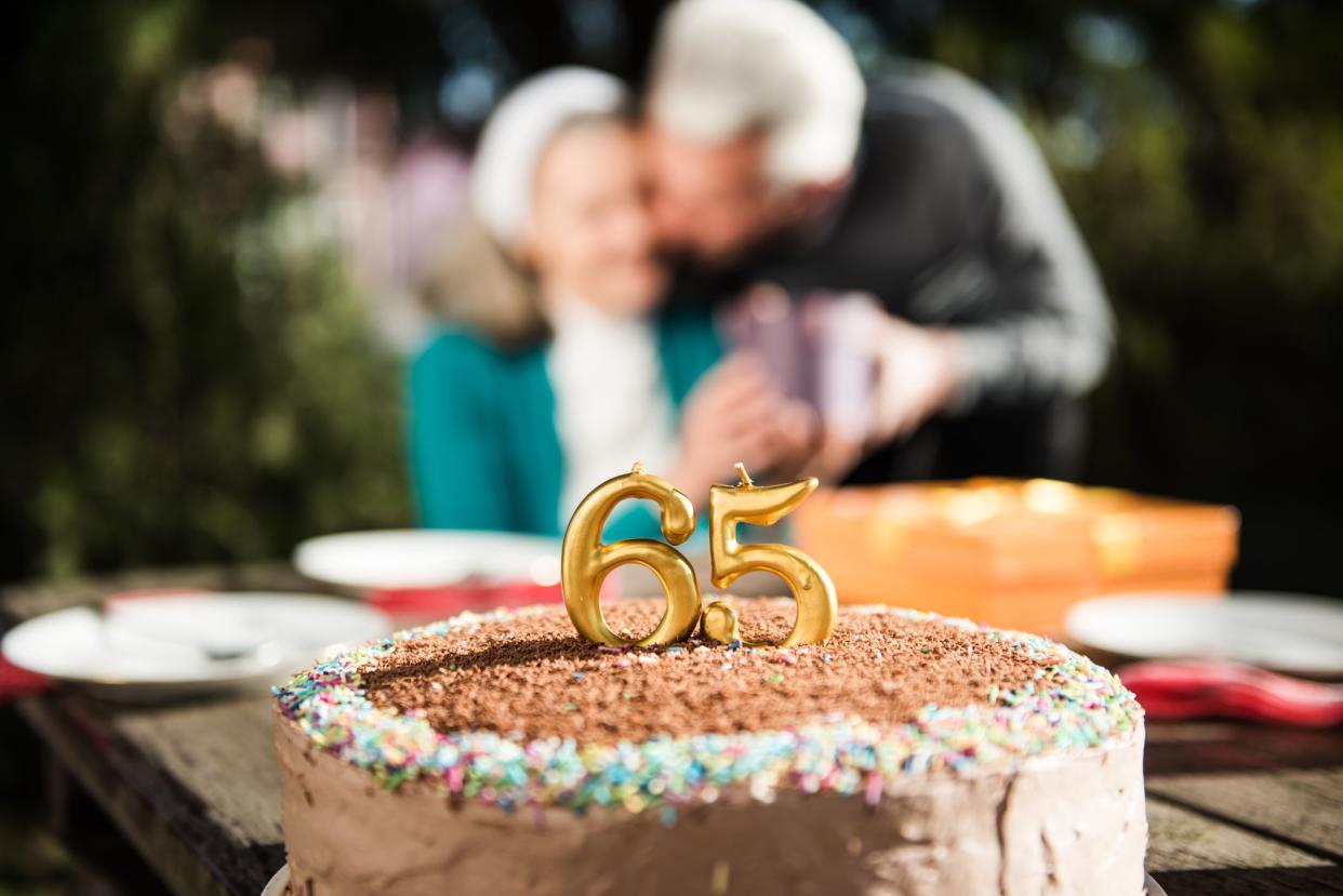 Happy senior woman receiving present from her husband on a birthday party at home backyard. Husband kissing his wife