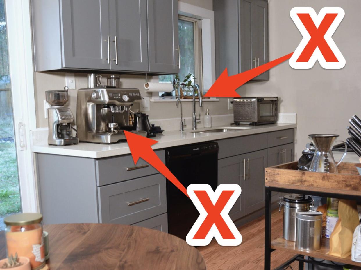 Gray cabinets in kitchen with wood floors with an "X" drawn pointing to a coffee maker on counter and to clutter on window ledge above faucet