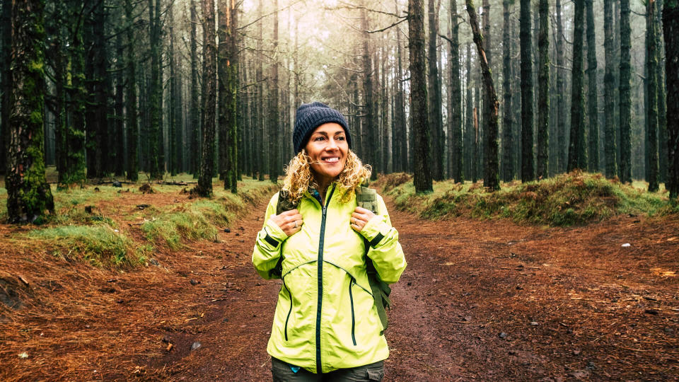 Happy hiker caucasian woman smile and enjoy the nature walking in a forest with high trees - alternative outdoor leisure activity and vacation lifestyle - sun in backlight and mist concept.