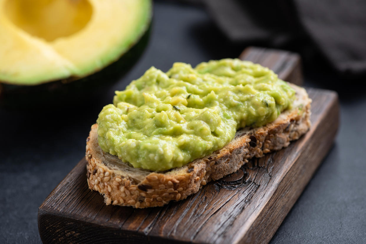 Mashed avocado on toasted multigrain bread served on wooden cutting board, closeup view