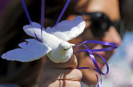 Jennifer Gordon holds a fabric dove at the base of balloons as she pays tribute to musician Prince at a makeshift memorial outside the fence of Paisley Park, his home and recording studio in Chanhassen, Minnesota, U.S., April 22, 2016. REUTERS/Eric Miller