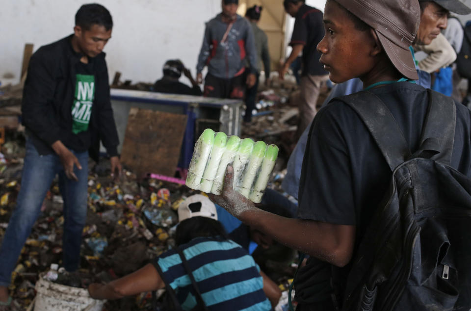 A man holds bottles of body lotion scavenged from an abandoned warehouse following an earthquake and tsunami in Palu, Central Sulawesi, Indonesia Indonesia, Wednesday, Oct. 3, 2018. Clambering over the reeking pile of sodden food or staking out a patch of territory, people who had come from devastated neighborhoods and elsewhere in the remote Indonesian city pulled out small cartons of milk, soft drinks, rice, candy and painkillers from the pile as they scavenge for anything edible in the warehouse that tsunami waves had pounded. (AP Photo/Dita Alangkara)