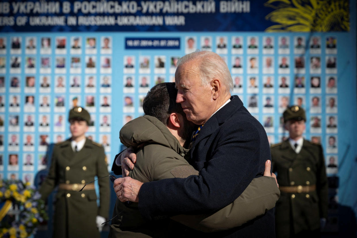 President Biden embraces President Volodymyr Zelensky in front of a wall carrying the images of lost Ukrainians.