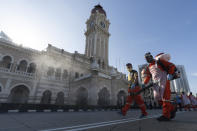 City hall workers spray a disinfectant at Merdeka Square, or independence square, situated in front of the Sultan Abdul Samad Building, background, in Kuala Lumpur, Malaysia, Saturday, Oct. 17, 2020. Malaysia will restrict movements in its biggest city Kuala Lumpur, neighboring Selangor state and the administrative capital of Putrajaya from Wednesday in an attempt to curb a sharp rise in coronavirus cases. (AP Photo/Vincent Thian)