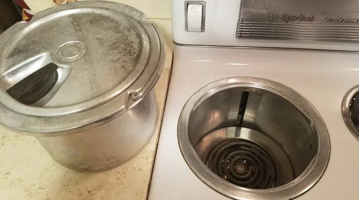 Large metal pot with lid next to a stove. An empty, round heating element is built into the surface of the stove