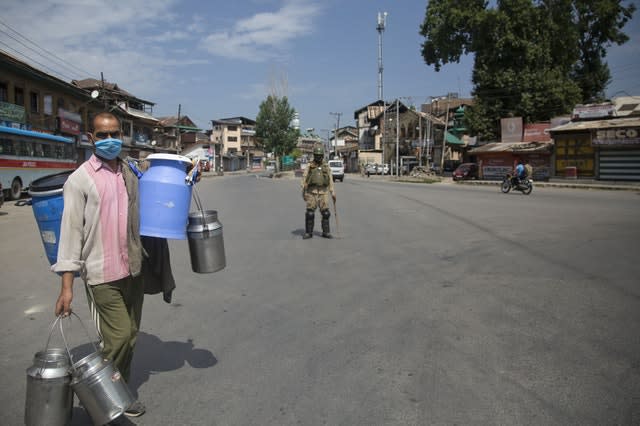 IA Kashmiri milkman walks past a paramilitary soldier during curfew (Mukhtar Khan/AP)