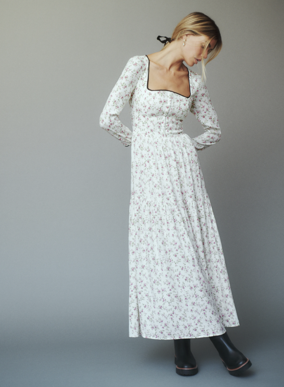 blonde model wearing black boots and long white and pink floral Chaylyn Dress with long sleeves and black trim (photo via Reformation)