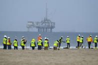 FILE - Workers in protective suits continue to clean the contaminated beach with a platform in the background in Huntington Beach, Calif., on Oct. 11, 2021. Federal regulators on Tuesday, Dec. 5, 2023, concluded the 2021 rupture of an undersea oil pipeline off the Southern California coast was likely caused by the proximity of anchored shipping vessels. (AP Photo/Ringo H.W. Chiu, File)