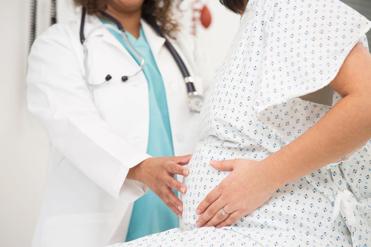 <p>Ariel Skelley/Getty</p> Stock image of a pregnant woman being examined by a doctor