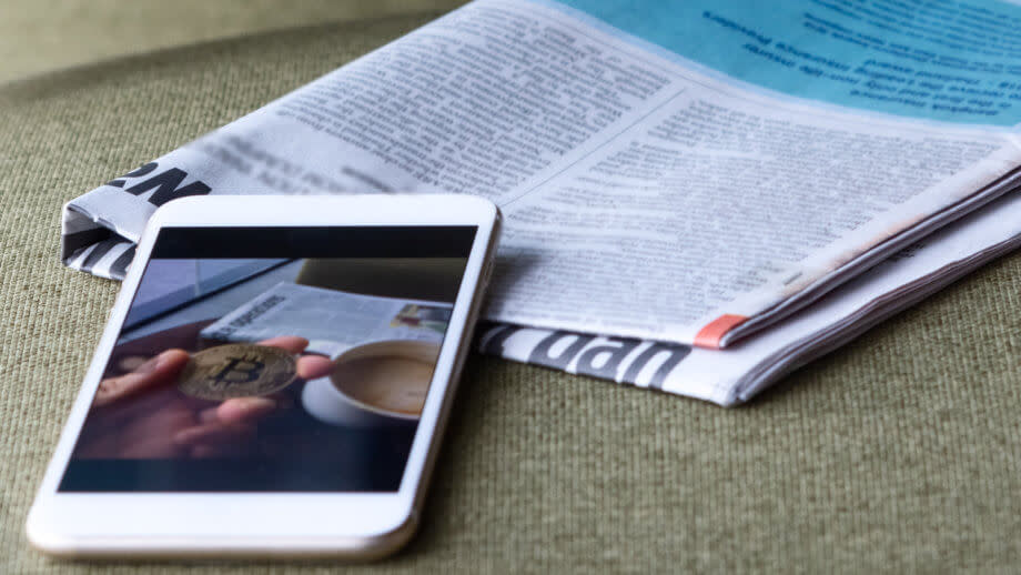 ein smartphone auf dem eine bitcoin münze und eine tasse kaffe gezeigt wird liegt auf einem tisch bei einer zeitung