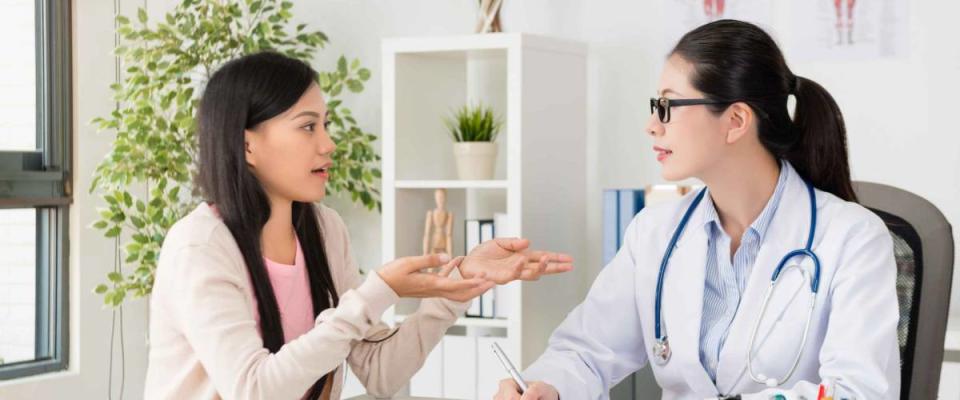 Young woman speaking to doctor, gesturing with her hands.