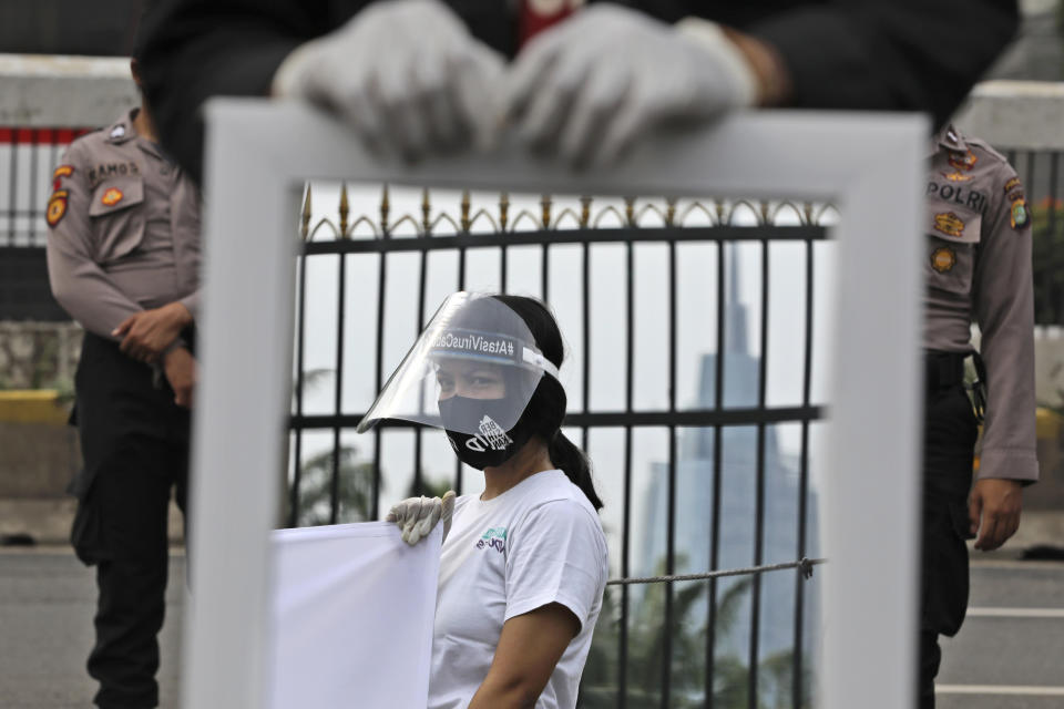 A mirror reflects the image of an activist wearing a mask and protective face shield as a precaution against the new coronavirus outbreak during a small protest outside the parliament in Jakarta, Indonesia, Tuesday, July 14, 2020. About a dozen activists staged the protest opposing the government's omnibus bill on job creation that was intended to boost economic growth and create jobs, saying that it undermined labor rights and environmental protection. (AP Photo/Dita Alangkara)