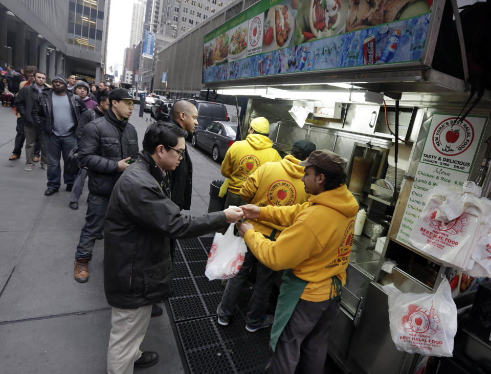 This Dec. 5, 2013 photo shows a line of people waiting to order from the popular sidewalk halal food cart near New York's Rockefeller Center. Rockefeller Center is crowded at Christmastime thanks to the famous tree, the skating rink and the show at Radio City Music Hall, but visitors can choose from a variety of places to eat in the area, from ethnic food and street carts to sit-down dining. (AP Photo/Richard Drew)